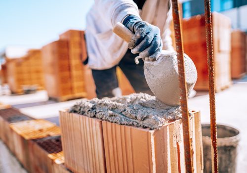 Bricklayer industrial worker installing brick masonry on exterior wall with trowel putty knife