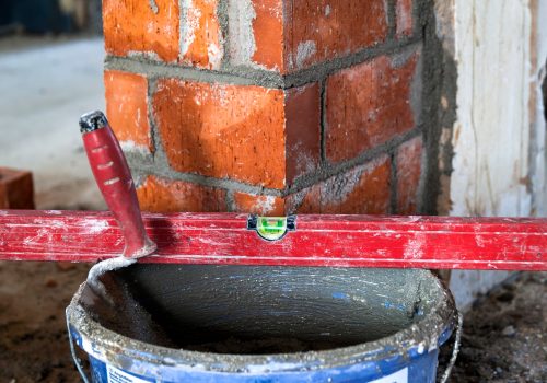 Close up of bricklaying industrial installing bricks on construction site wall with working tools