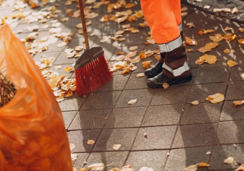Janitor cleaner sweeping autumn leaves on the street