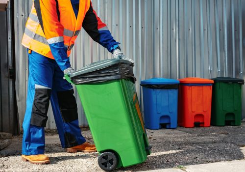 Male janitor in uniform cleans a trash can in the street